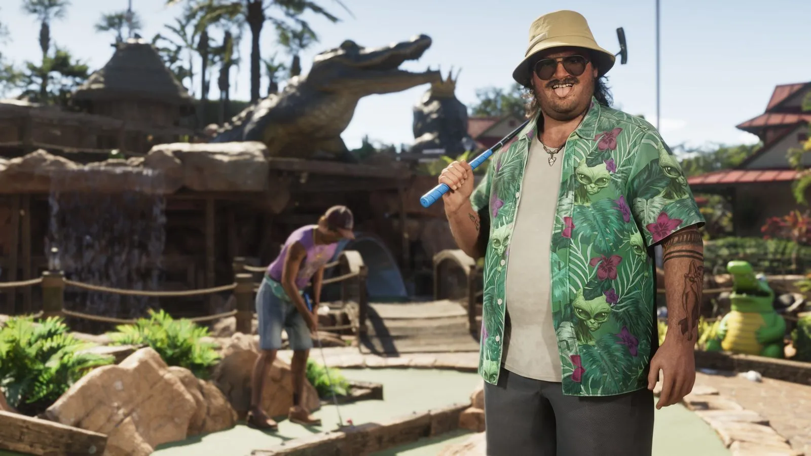 Cal Hampton in an oversized green short-sleeve button-up printed with hibiscus, monstera leaves and cartoon alien heads, paired with a khaki bucket hat and aviators