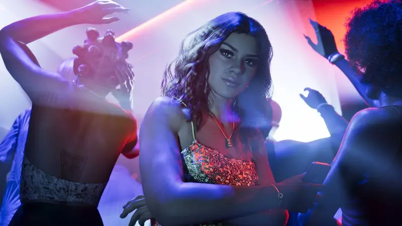 Lucia Caminos in a metallic gold sequin cami catching red and purple neon lighting on a Vice City nightclub dancefloor